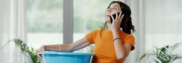 woman calling for leak repair assistance while collecting leaking water