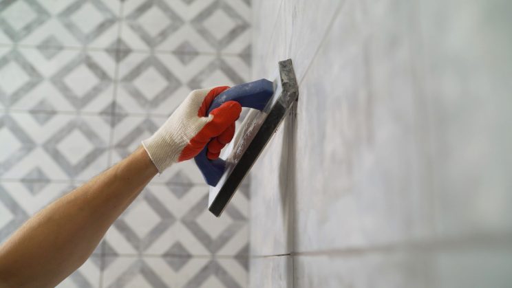 man's hand holding trowel against tiles